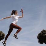 Athletic woman in action jump against a blue sky background. Captures fitness in motion.
